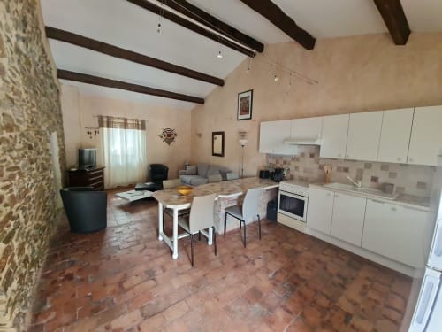 Cucina a vista e zona living del Gîte Le Tilleul con pavimento in cotto, travi a vista e arredamento bianco