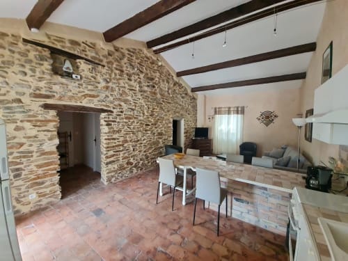 Sala da pranzo con muri in pietra, travi a vista, tavolo da pranzo, angolo cucina e accesso allo spazio abitativo presso Chambre d'hôtes Gîte