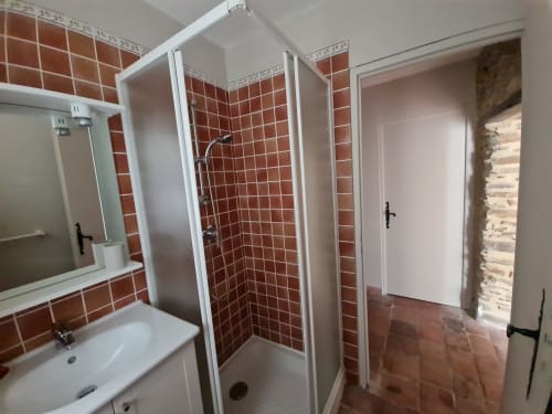 Bagno moderno con pareti in piastrelle rosse, lavabo bianco, specchio e doccia presso la Chambre d'hôtes Gîte Le Tilleul