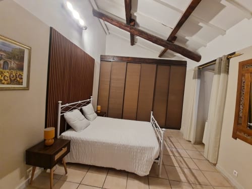 Camera da letto luminosa con letto in metallo bianco, travi a vista, armadio marrone e pavimento piastrellato.