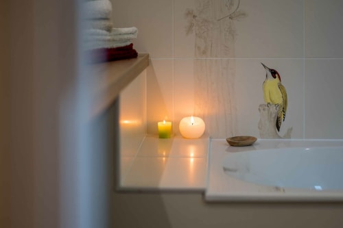 Serene spa-like bathroom detail at L'Amiradou B&B, featuring lit candles, bird artwork, and peaceful ambiance in