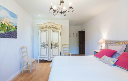 Spacious bedroom at L'Amiradou B&B with ornate white wardrobe, pink bedding, wooden floors and artistic décor in