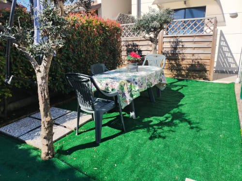 Sunny garden patio at Casa Meravigliosa with dining table, artificial turf, potted plants and wooden privacy screens in