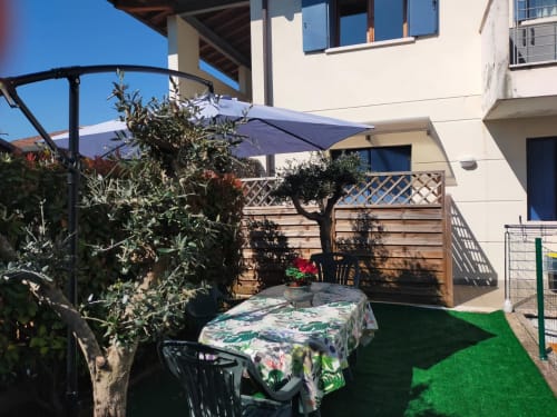 Sunny garden patio at Casa Meravigliosa with table, olive tree, blue umbrella, and wooden fence in Fontanafredda
