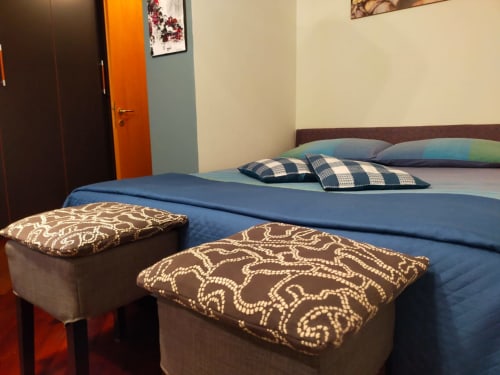 Modern bedroom at Casa Meravigliosa featuring blue bed with decorative pillows and patterned ottomans, orange door,