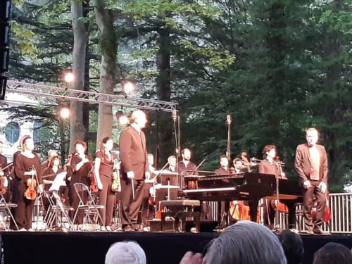 Outdoor orchestra performance among tall trees at L'Amiradou in Félines-sur-Rimandoule, France.