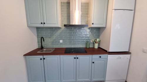 Cozinha moderna do apartamento Casa da Oliveirinha com armários azul claro, bancada em madeira escura, fogão a gás e azulejos verdes