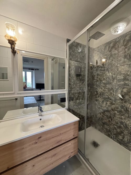 Bagno moderno nell'appartamento milanese con mobile in legno, specchio grande, doccia walk-in decorata e piastrelle bianche