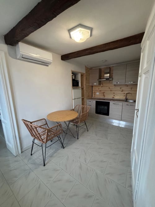 Zona cucina-pranzo moderna nell'Apartment Sormano 3 con tavolo in legno, sedie in vimini, angolo cottura attrezzato e travi a vista