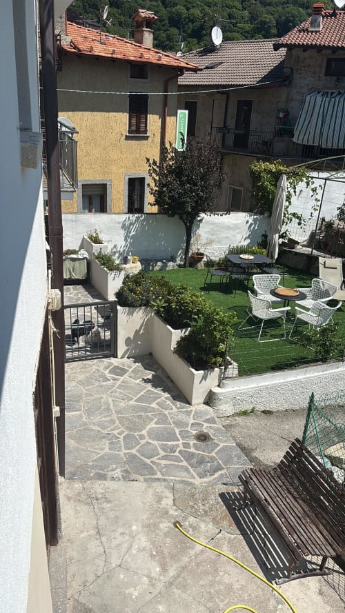 Cortile dell'Appartamento Sormano 3 con prato verde, zona lounge bianca, piante in vaso e panorama dei palazzi storici di Milano