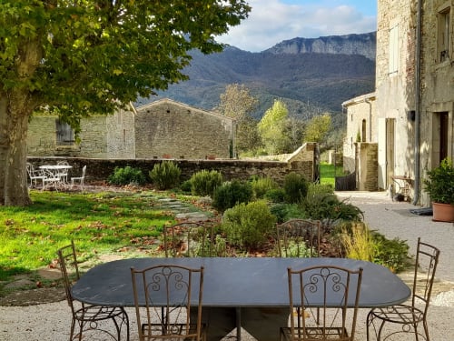 Cour de L'Amiradou avec table à manger, bâtiments en pierre et vue sur les montagnes à Félines-sur-Rimandoule