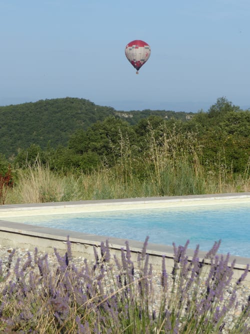 Hot air balloon floating above L'Amiradou's pool with lavender gardens and Félines-sur-Rimandoule landscape