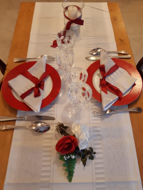 Élégante table dressée à la L'Amiradou B&B avec assiettes rouges, serviettes blanches, verres en cristal et rose rouge.