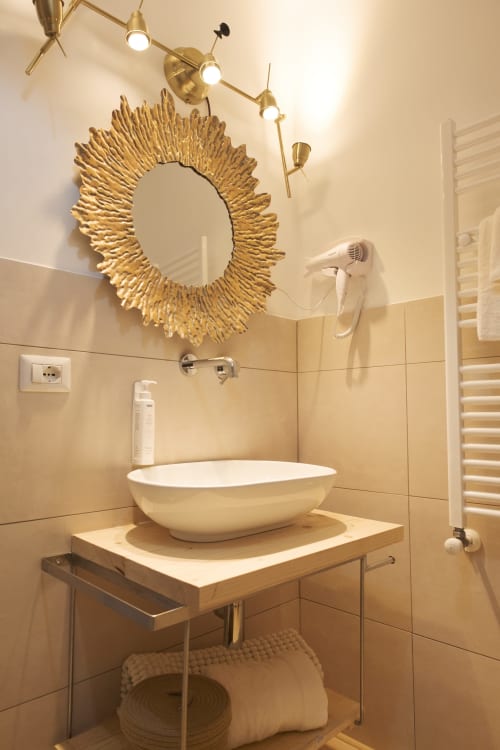 Bagno moderno dell'hotel Cuore di Rocca a Rocca di Papa con lavabo baciato, specchio a raggi dorati e rubinetteria in ottone
