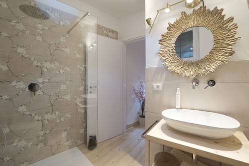 Bagno moderno all'Hotel Cuore di Rocca a Rocca di Papa con piastrelle floreali decorative, lavabo a coppa e specchio dorato a raggiera