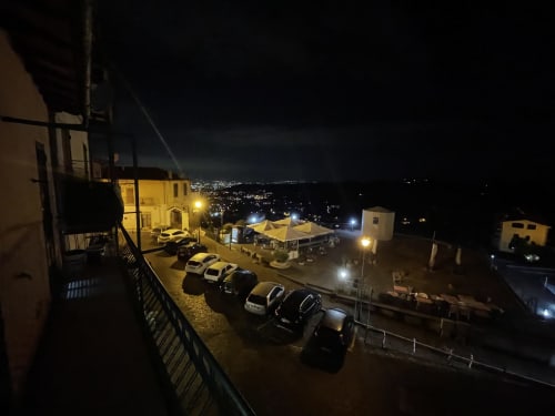 Vista notturna dall'hotel Cuore di Rocca a Rocca di Papa: cortile illuminato, auto parcheggiate e luci della cittadina sui colli