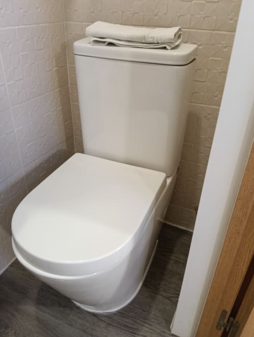 Modern white toilet with closed seat and folded towel on tank in Vila Alexandra hostel room, Costa da Caparica