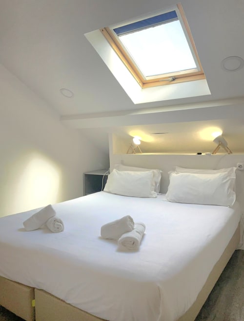Modern bedroom at Vila Alexandra hostel with skylight, queen bed, white bedding, rolled towels, and wall sconces in Costa da
