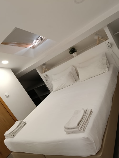 Bright bedroom at Vila Alexandra hostel in Costa da Caparica with white bed, skylight, shelving, and modern amenities