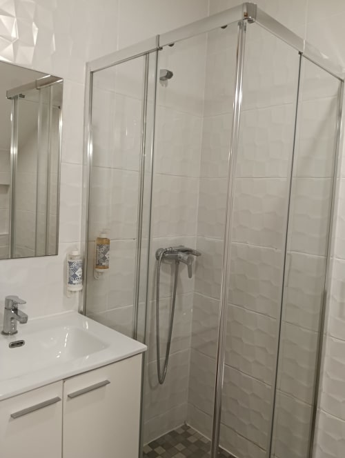 Modern bathroom at Vila Alexandra hostel in Costa da Caparica with glass shower enclosure and white tile walls