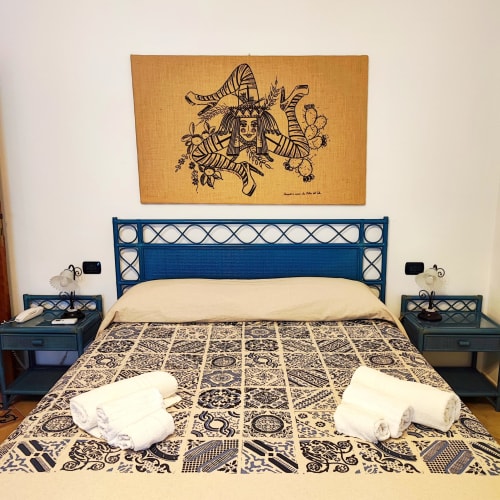 Camera Tripla dell'Hotel Principe di Rinella con letto in metallo blu, biancheria a motivi, asciugamani bianchi e opere d'arte egiziana