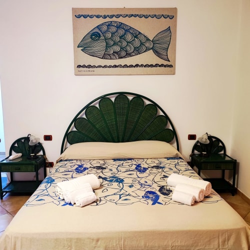 Camera quadrupla all'Hotel Principe di Rinella con testata decorativa a ventaglio verde, quadri di pesci e asciugamani bianchi sul letto