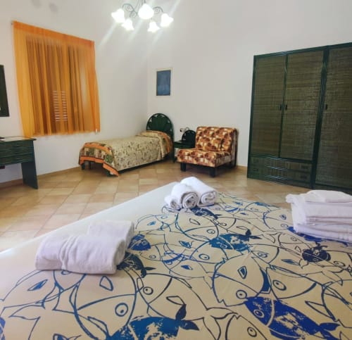 Ampia camera quadrupla all'Hotel Principe di Rinella con più letti, armadio verde, tende arancioni e pavimentazione in piastrelle.