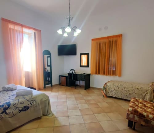 Ampia camera quadrupla all'Hotel Principe di Rinella con letti gemelli, divano letto, scrivania, TV e pavimento in cotto