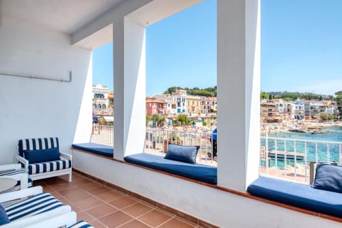 Coastal terrace with striped seating overlooking colorful buildings and Mediterranean beach in Palafrugell