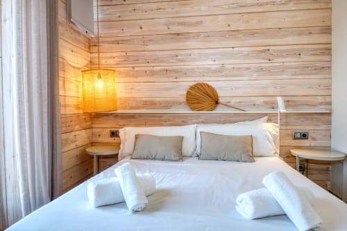 Modern wooden bedroom at Finques Garcia Enrich in Palafrugell with white bedding, pendant lamp, and minimalist decor.