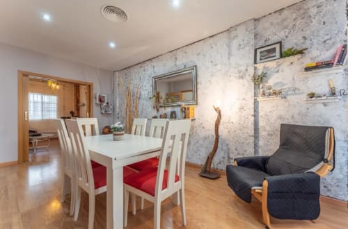 Comedor y sala de estar tipo cabaña moderna en Mérida con mesa de comedor blanca, sillón negro y estantes decorativos
