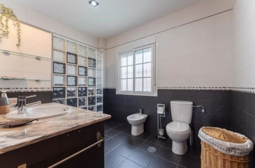 Baño moderno con azulejos blanco y negro, lavamanos, inodoro, bidé y bloques de vidrio decorativo en la casita de Mérida