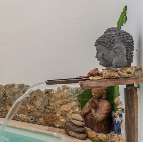 Estatua de Buda y escultura de monje junto a la piscina en la cabaña Gestyp-AT de Mérida, con rocas decorativas y plantas