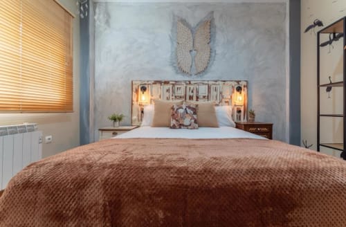 Dormitorio de cabaña moderna en Gestyp-AT, Mérida, con manta terracota, cabecero iluminado y cuadros de alas