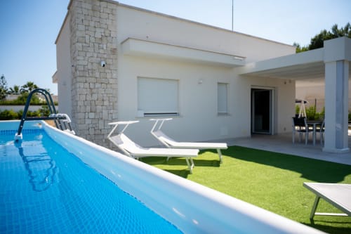 Modern white villa with pool, lounge chairs, and patio in Ferrara, Italy