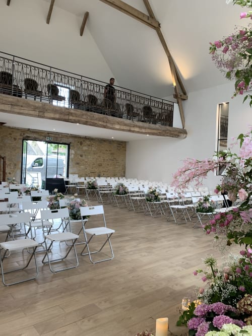 Cérémonie de mariage élégante au Château de Baylac avec chaises blanches, fleurs roses et poutres apparentes