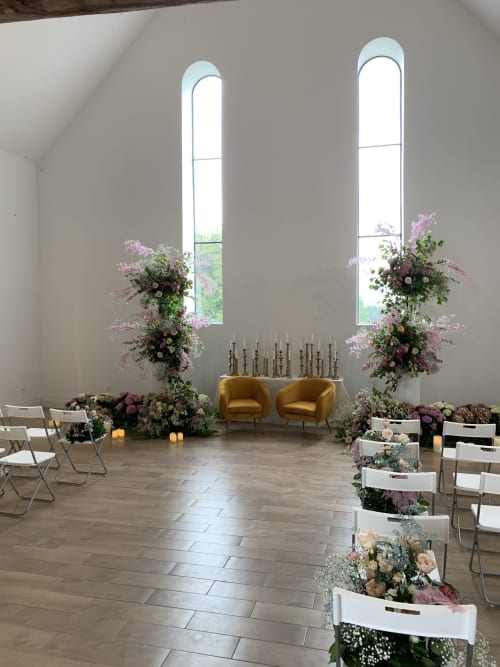 Cérémonie de mariage élégante au Château de Baylac avec fleurs roses, chaises dorées et grandes baies vitrées en arc