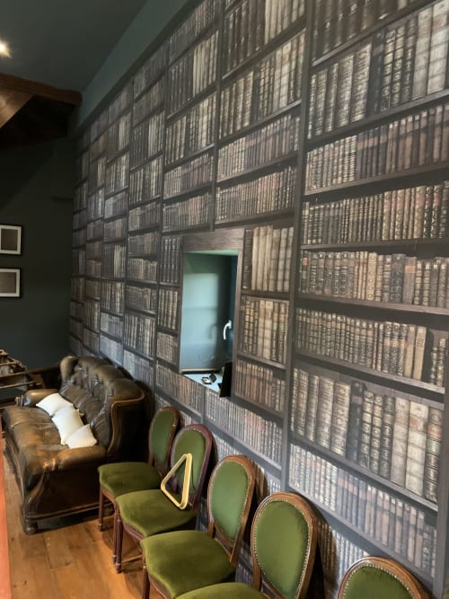 Salon bibliothèque du Château de Baylac avec canapé en cuir, chaises vertes et mur de livres du sol au plafond