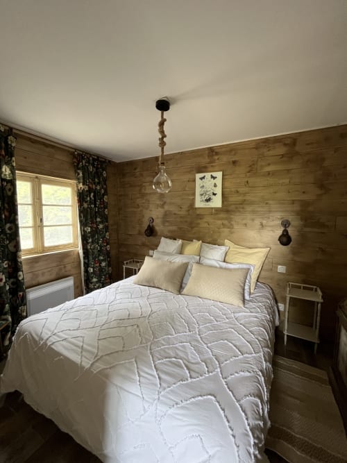 Chambre cosy en bois aux Papillons de Baccara avec literie matelassée blanche, oreillers jaunes et vue sur le jardin