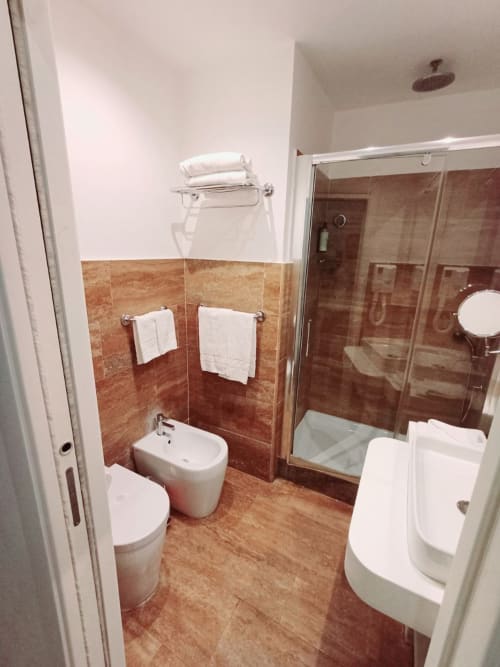 Bagno moderno nella Michelangelo Suite Roma con pavimento in cotto, cabina doccia, bidet, wc e sanitari bianchi