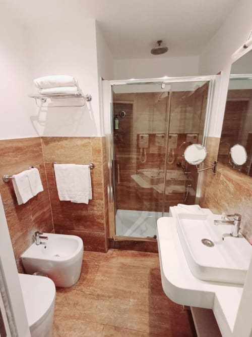 Bagno moderno della Michelangelo Suite Roma con doppio lavabo, doccia con box in vetro e finiture in cotto caldo