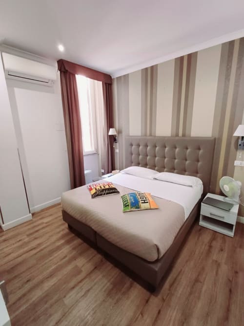 Camera moderna della Michelangelo Suite Roma con letto matrimoniale, carta da parati a righe, tende bordeaux e pavimento in legno