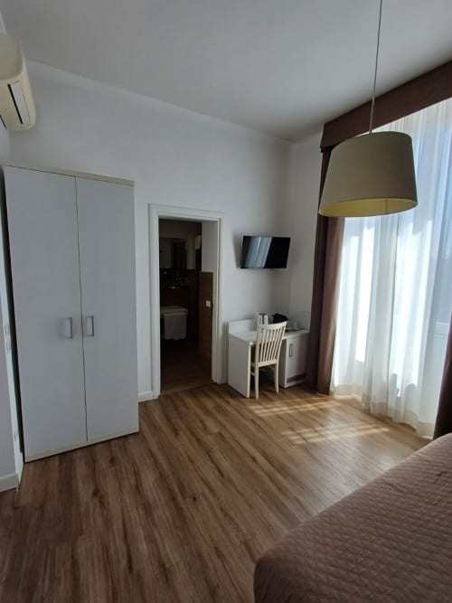Camera moderna della Michelangelo Suite Roma con armadio bianco, scrivania, lampada a sospensione, parquet e vista giardino