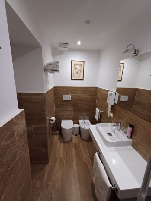 Bagno moderno della Michelangelo Suite Roma con piastrelle marroni, lavabo bianco, WC, bidet e vasca nella camera tripla King