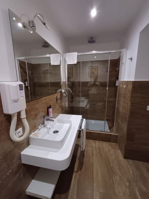 Bagno moderno della Michelangelo Suite Roma con lavabo bianco, ampia doccia e dettagli in piastrelle marroni
