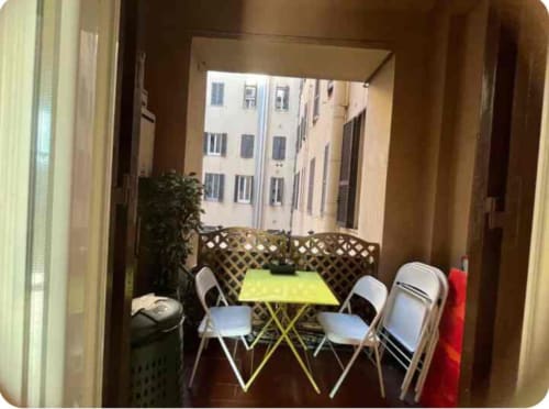 Balcone compatto della Michelangelo Suite Roma con tavolo giallo, sedie bianche e vista sulla corte