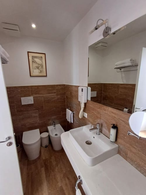 Bagno moderno presso Michelangelo Suite Roma con pareti in piastrelle marroni, lavabo bianco, toilette e specchio