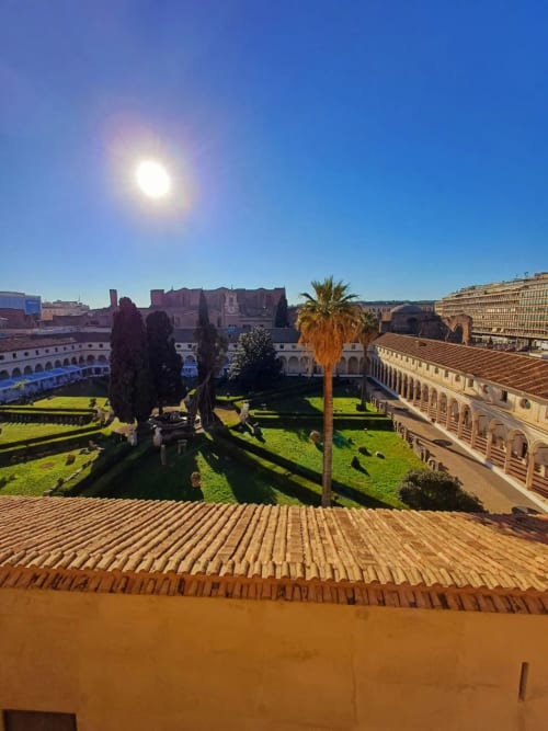 Giornata di sole nel giardino del chiostro Michelangelo della Michelangelo Suite Roma, con palme e architettura storica