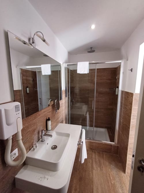 Bagno moderno della Michelangelo Suite Roma con doppio lavabo, grande specchio, doccia walk-in con piastrelle in legno e scaldasalviette