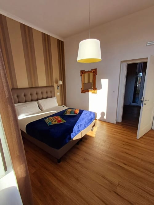 Camera da letto matrimoniale moderna presso Michelangelo Suite Roma con biancheria blu, testata rigata, pavimento in legno e illuminazione a sospensione.